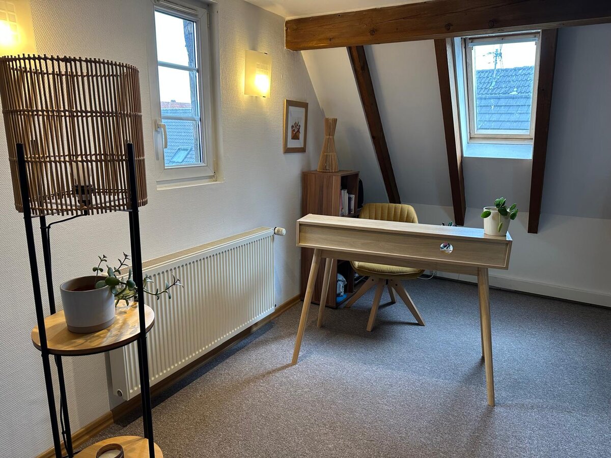 Le bureau de consultation d'Aurélie Roethinger — bureau en bois clair, fauteuil moutarde, lampe en rotin et plante.
