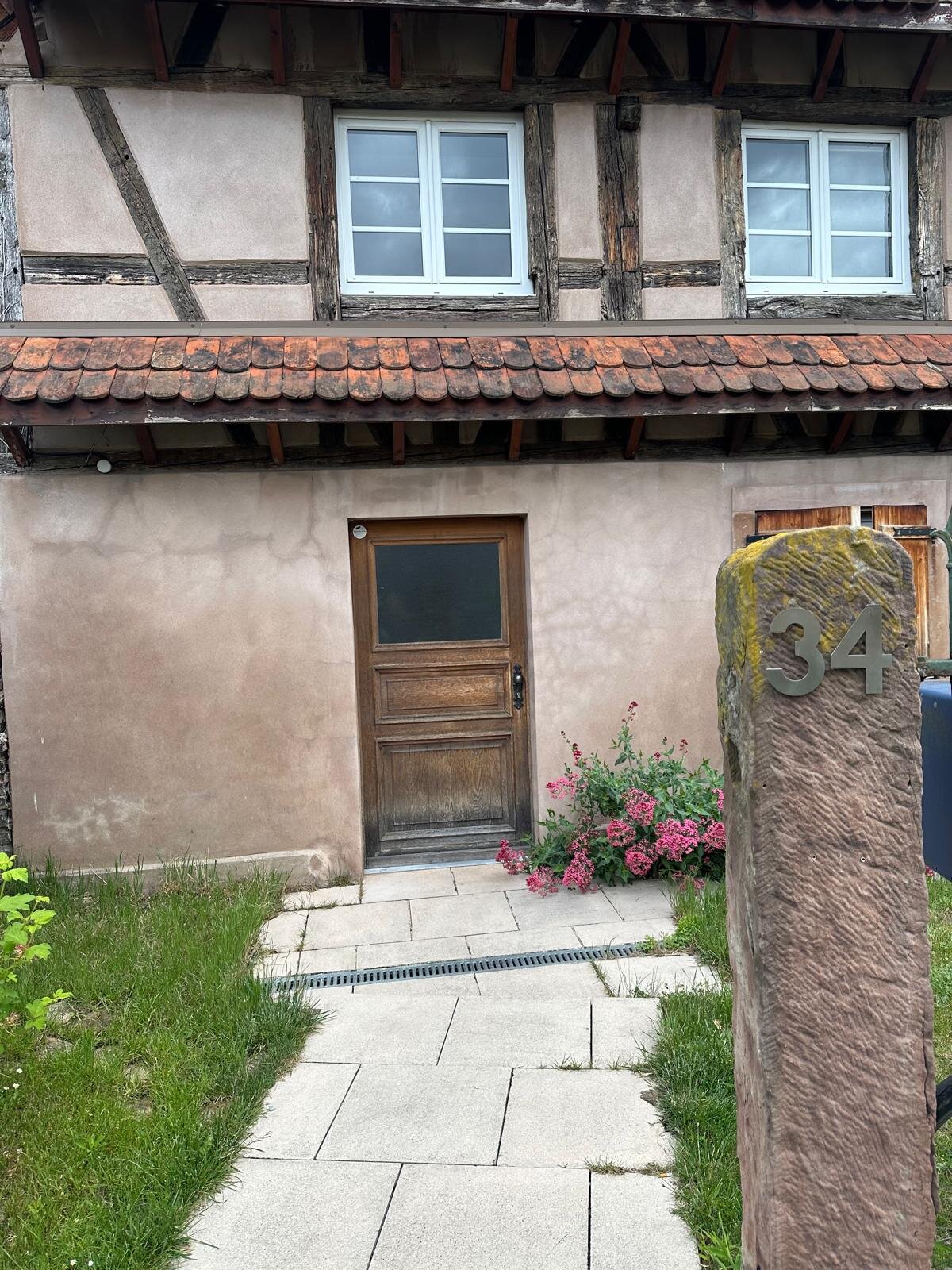 Entrée du cabinet — porte en bois sous l'auvent à tuiles anciennes, borne en pierre indiquant le numéro 34.